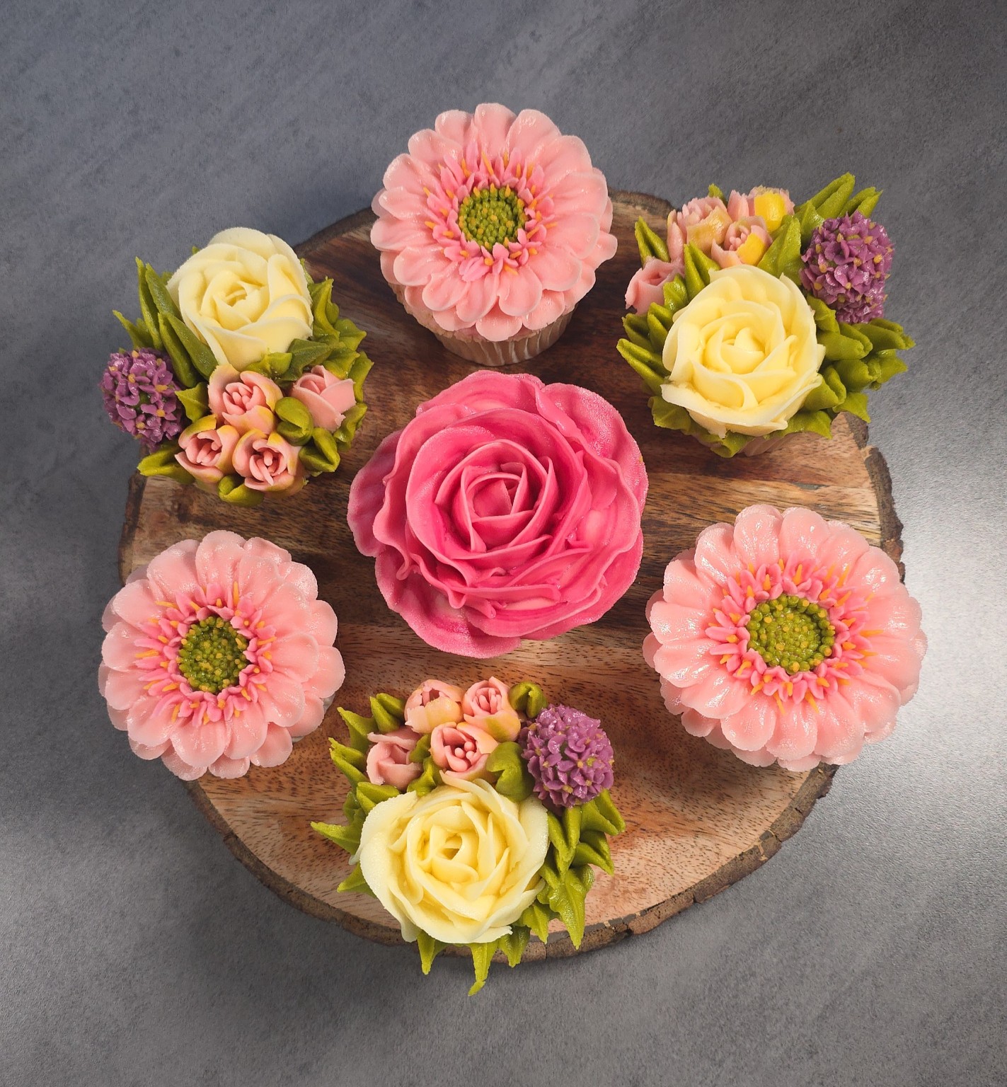 Pink and cream hand-piped floral cupcakes on a wooden board